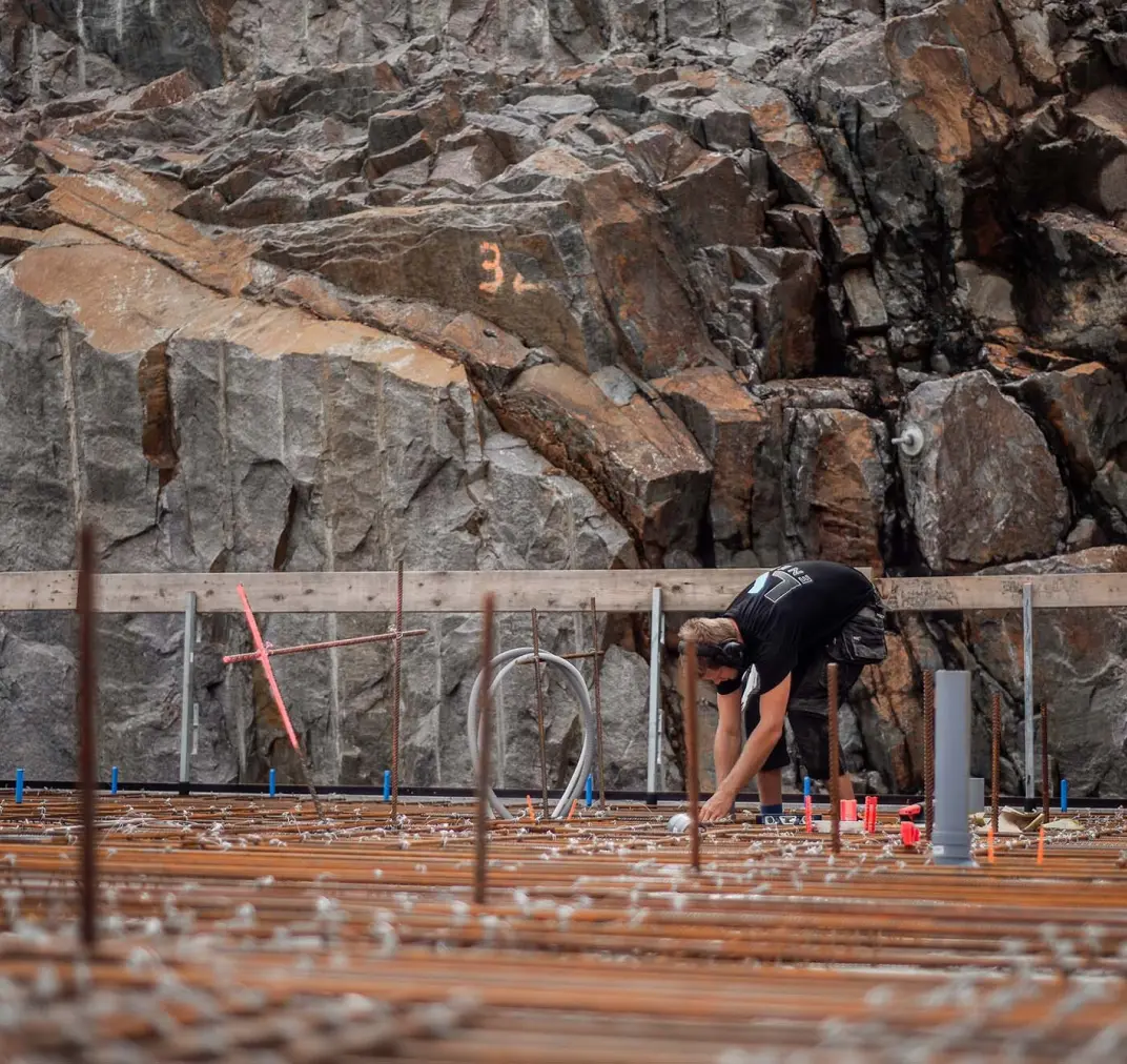 Montör böjer sig över armering vid bergvägg på byggarbetsplats