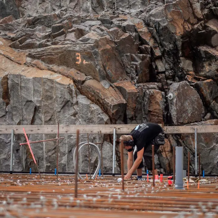 Montör böjer sig över armering vid bergvägg på byggarbetsplats